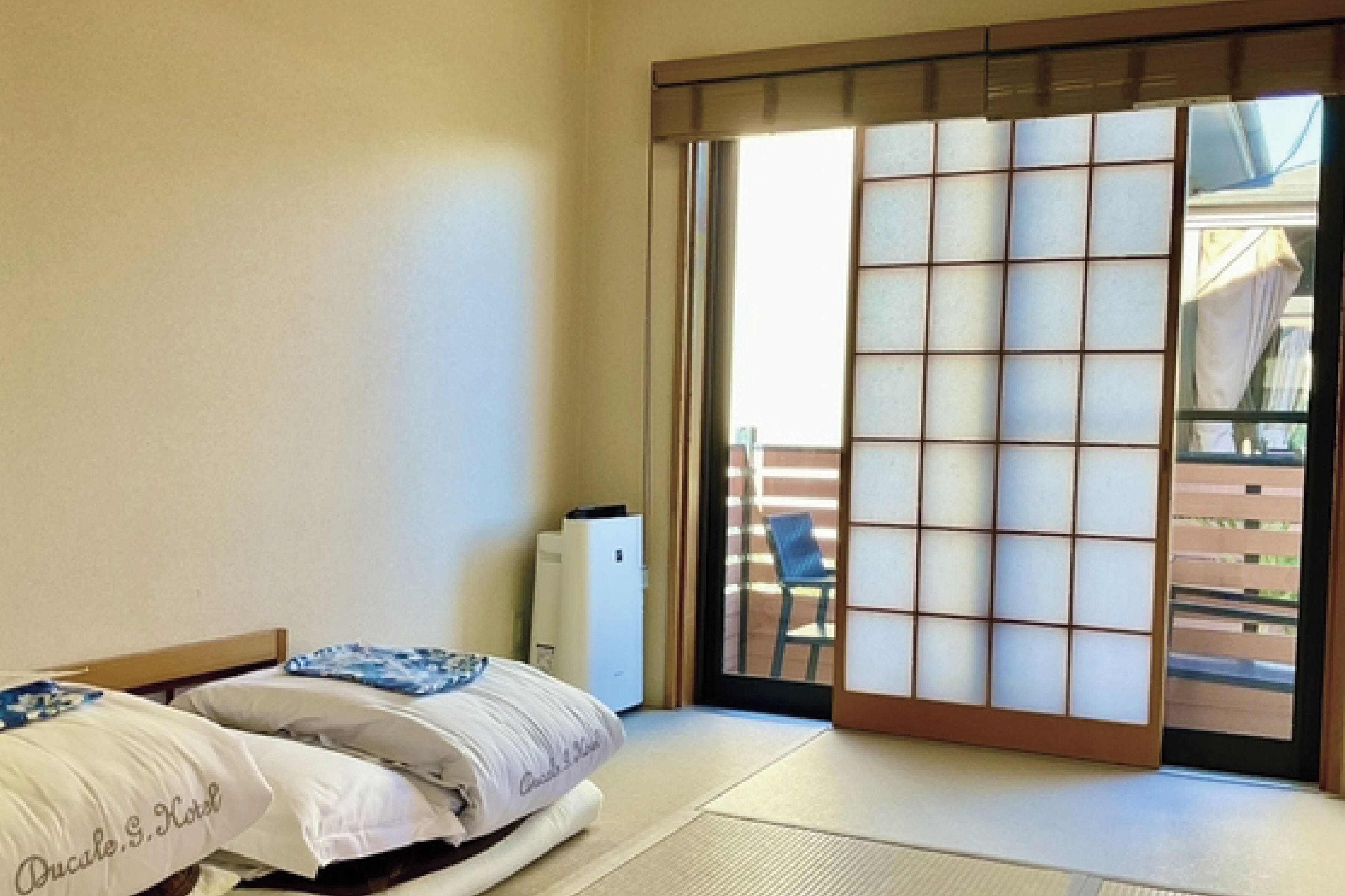 A room with two beds, a sliding shoji screen door, a small white appliance, and a view of a wooden deck outside.