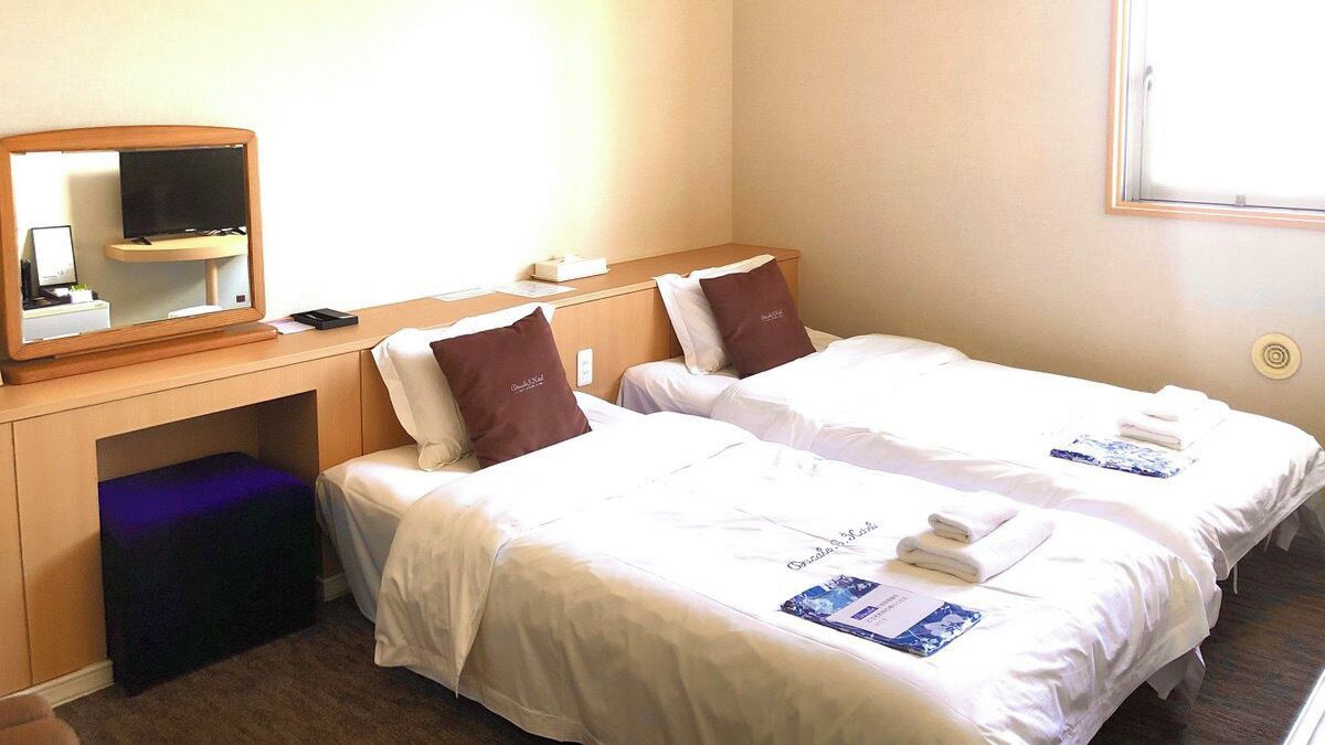 Een hotelkamer met twee bedden, een bureau met een computer, een spiegel en een raam.