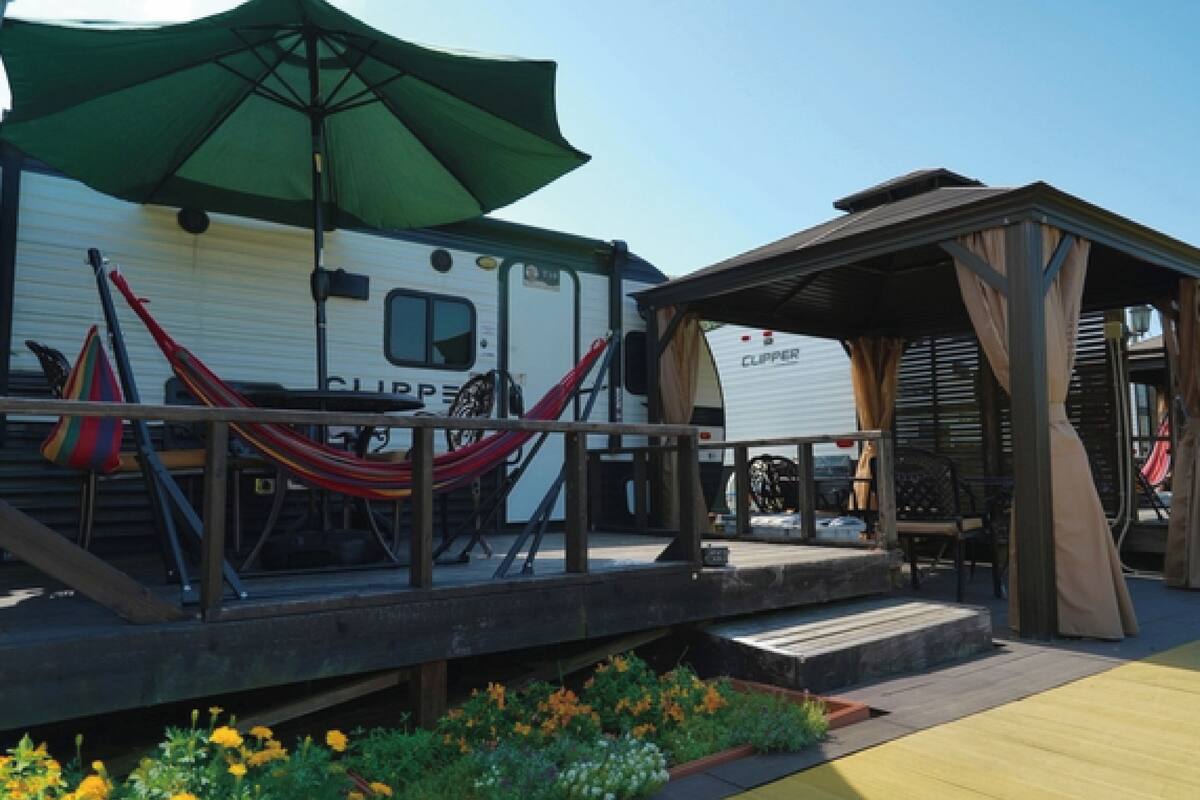 A mobile home with a covered patio area, a hammock, and a small deck with steps leading to the entrance.