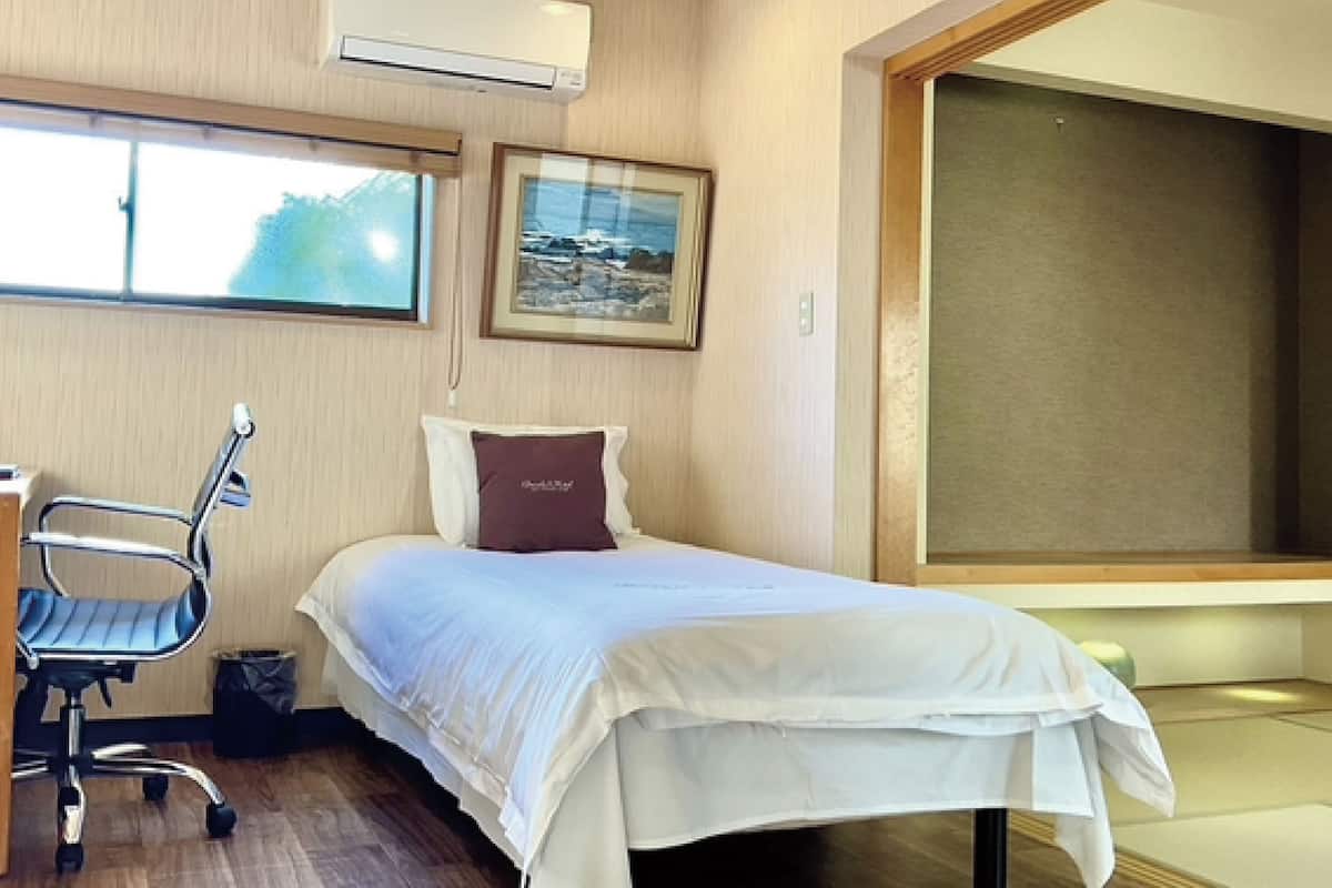 A hotel room with a bed, a desk, a chair, a picture on the wall, and a window.