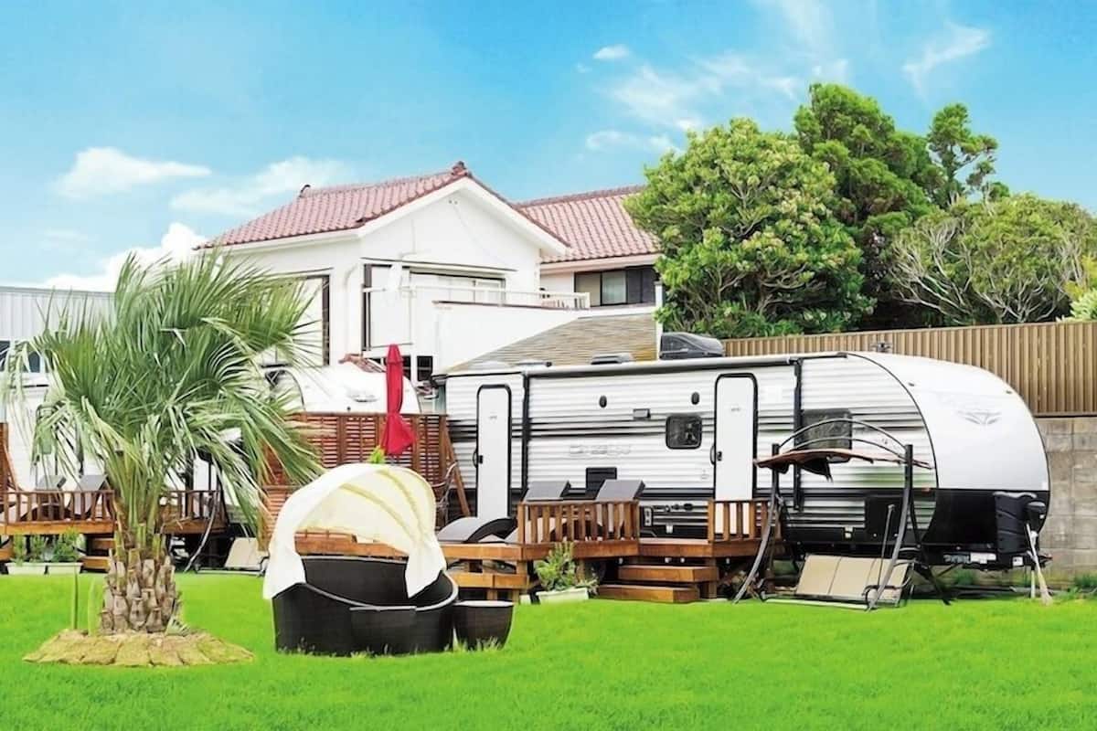 A recreational vehicle (RV) parked in a grassy area with a house in the background.