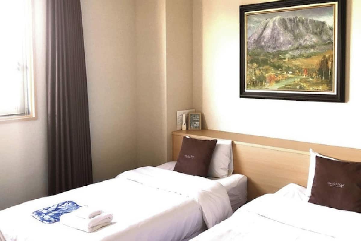 A hotel room with two beds, a painting on the wall, and a window with curtains.
