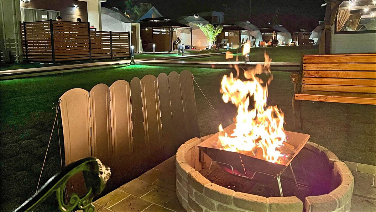 A fire pit with flames, surrounded by a wooden fence and a bench.