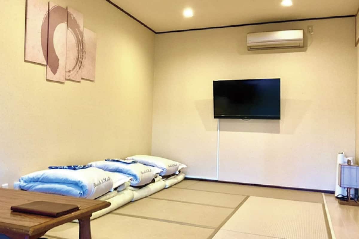 A room with a bed, a flat-screen TV mounted on the wall, a wooden table, and a tatami mat floor.