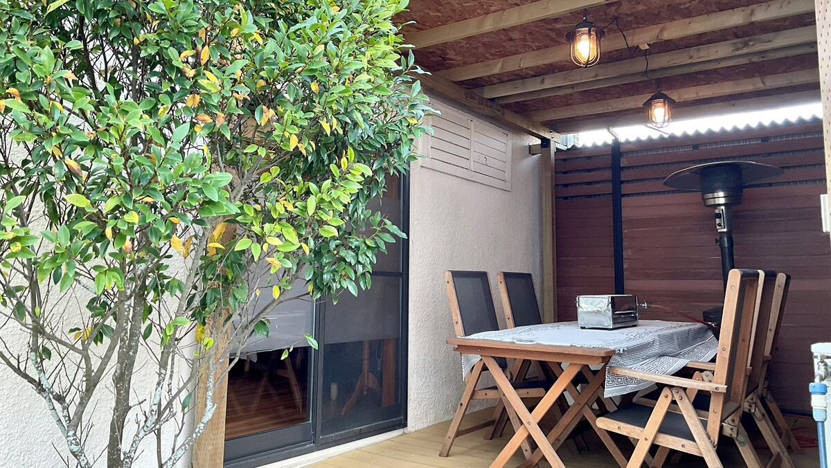 A patio with a table and chairs, a small tree, and a heater.
