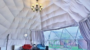 A tent-style room with a bed, a red chair, a blue chair, a table, and a chandelier. - Ducale Garden Hotel 99 (Kujukuri)