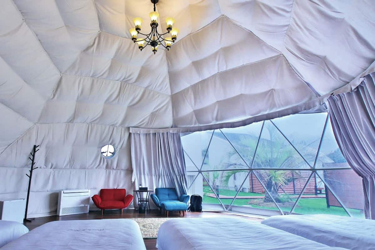 A tent-style room with a bed, a red chair, a blue chair, a table, and a chandelier.