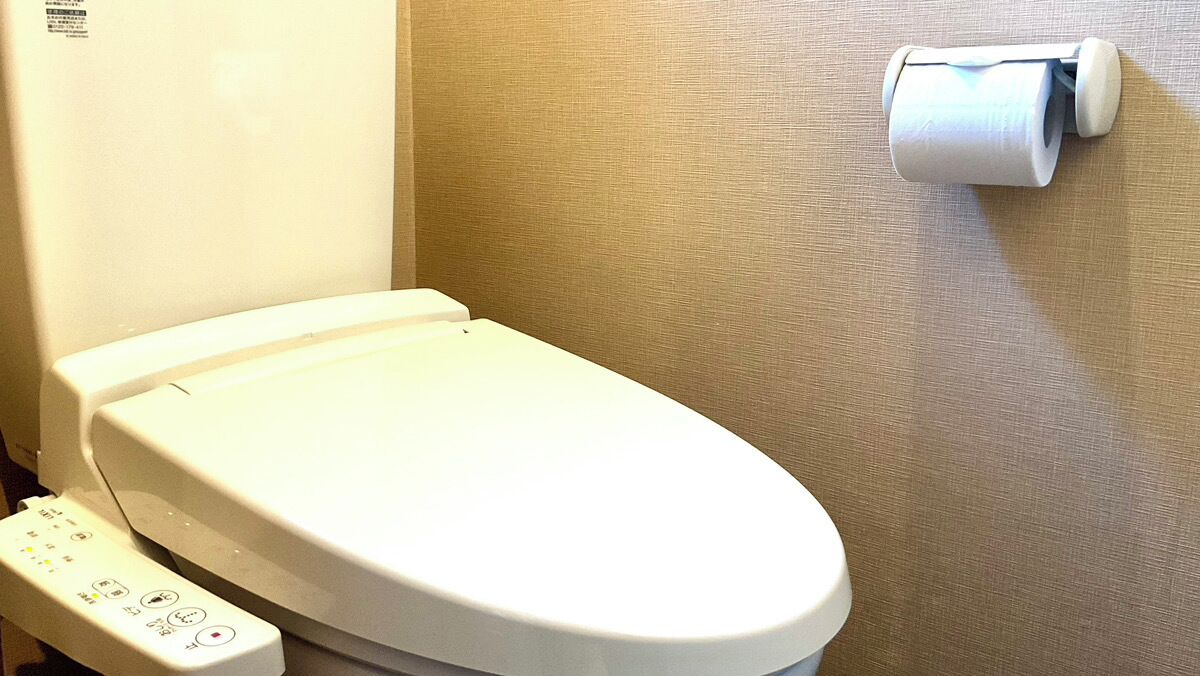 Un bagno con un pannello di controllo e un portasciugamani per carta igienica a parete.