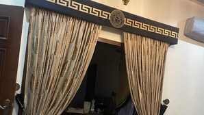 Una habitación con una puerta decorada con un motivo negro y dorado, una pequeña mesa con una silla, y una mesa de cristal en primer plano.