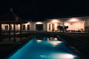 Una piscina con zona cubierta y un edificio con varias habitaciones y un perchero.