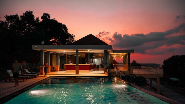 Un área moderna junto a la piscina con un mostrador de recepción, sillones de descanso y una piscina que refleja las luces.