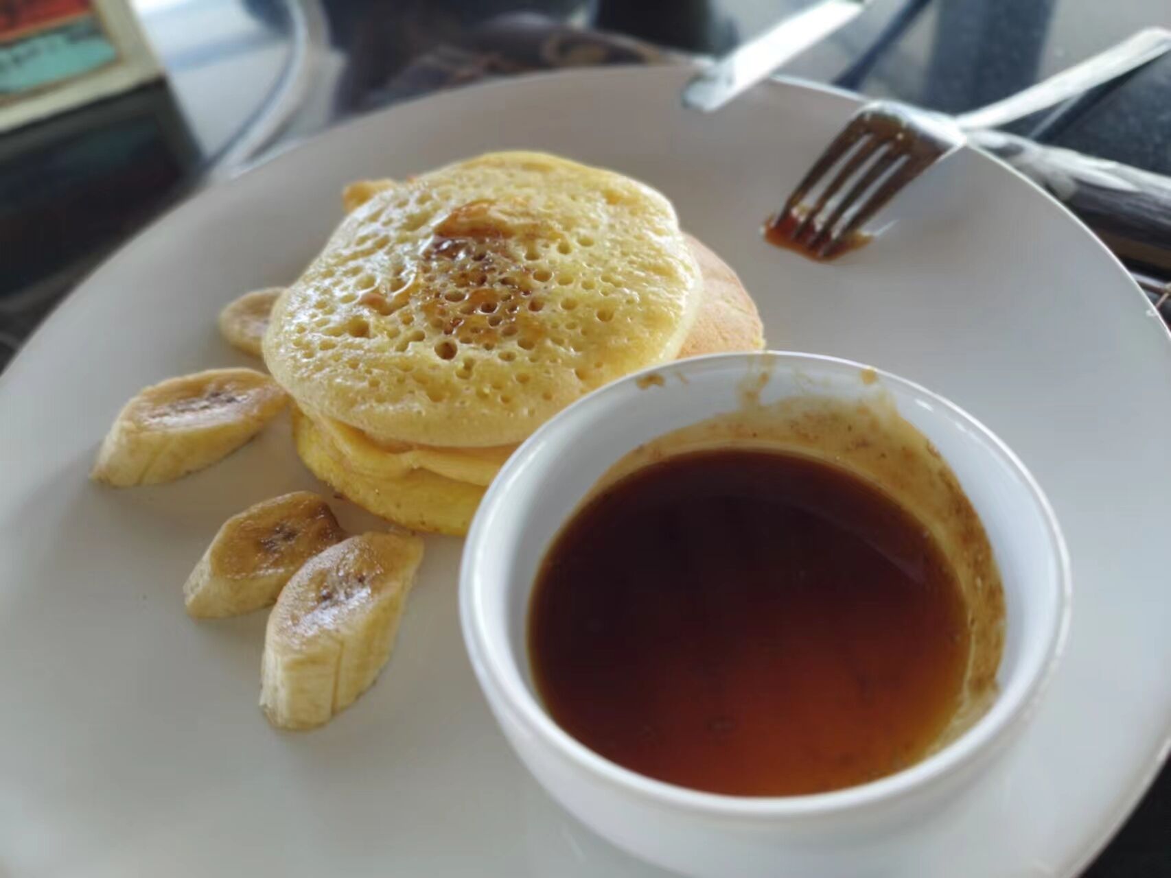 A plate with pancakes, syrup, and banana slices.