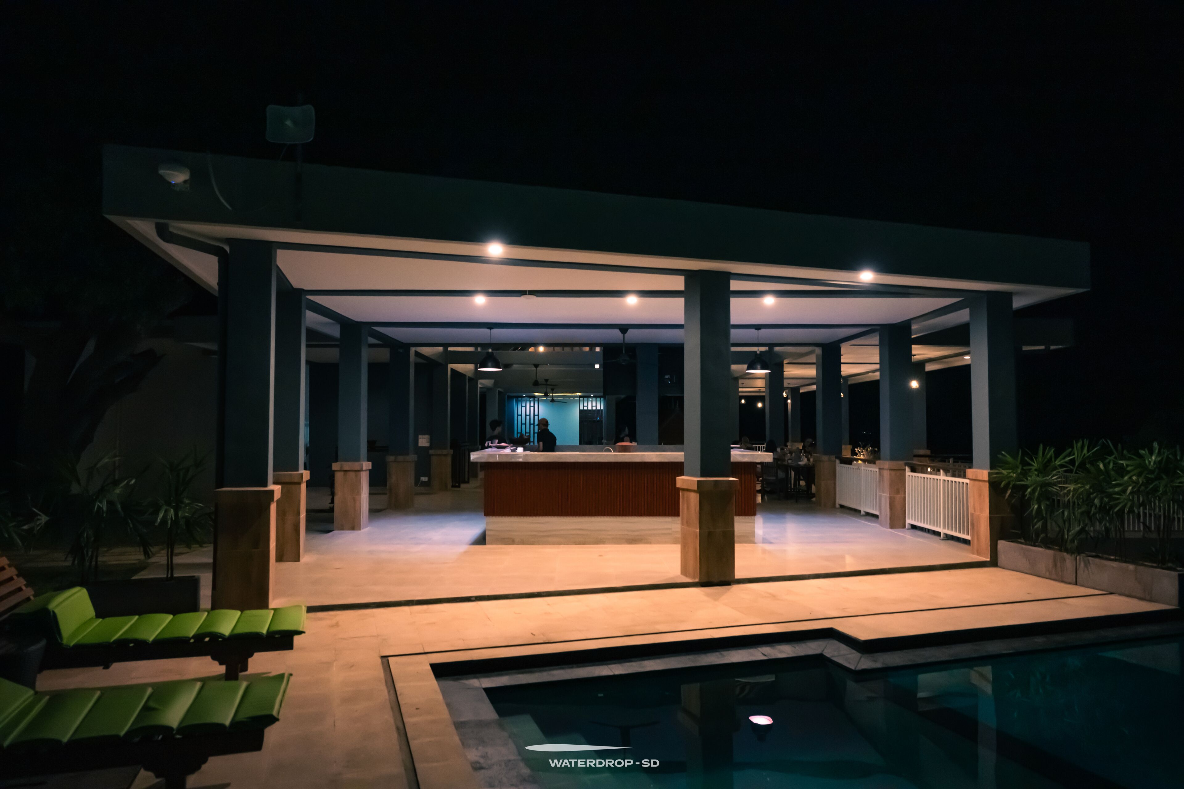 Area piscina moderna all'aperto con reception, poltrona relax e zona salotto coperta.
