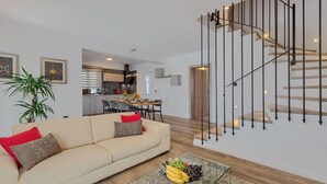 A modern living room with a sofa, a dining area, and a staircase.