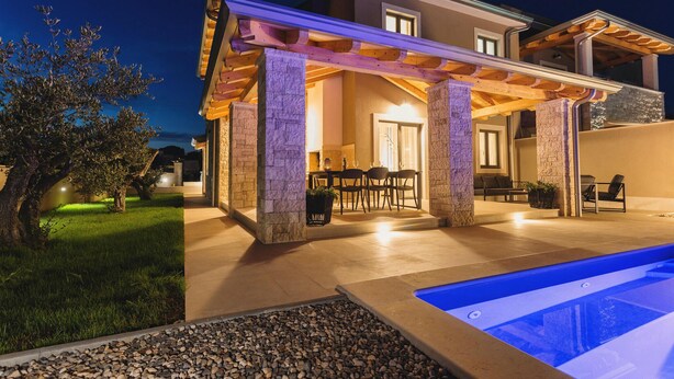A modern house with a covered patio, a pool, and a well-maintained garden.