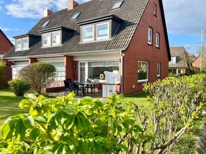 Une maison à deux étages dotée d’une grande véranda à l’avant, d’un coin repas avec mobilier d’extérieur et d’un jardin bien entretenu.