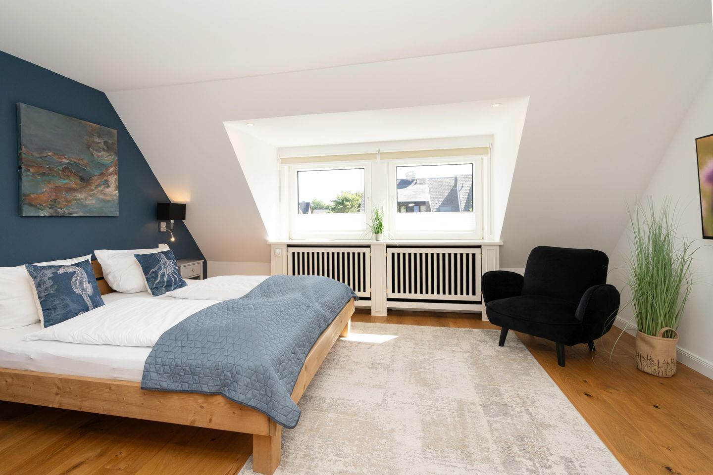 Ein Schlafzimmer mit einem Bett, einem schwarzen Sessel, einer Heizung und einem Fenster.