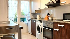 Une cuisine moderne équipée d’un lave-linge et d’un sèche-linge intégrés, un coin repas avec une table et des chaises, et une vue par la fenêtre.
