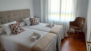 Une chambre d’hôtel avec deux lits, une chaise et une fenêtre avec des rideaux.