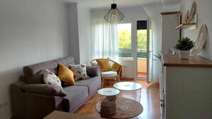 Un salon moderne comprenant un canapé, deux fauteuils, une table basse et une table à manger. On y trouve une fenêtre avec des rideaux, une porte donnant sur l’extérieur et une petite plante posée sur une étagère.