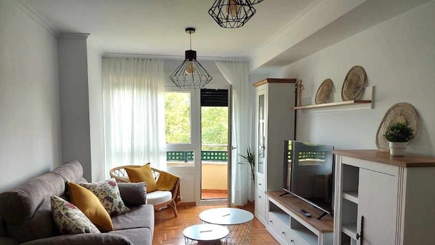 Un salon avec un canapé, deux tables rondes, un téléviseur et un balcon agrémenté de rideaux.