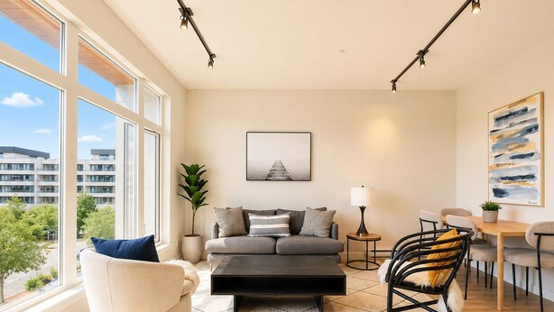A modern living room with a sofa, a chair, a coffee table, a TV, and a dining area with chairs and a table.