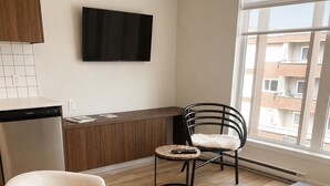 Un salon moderne comprenant un canapé, une table basse, un fauteuil, un téléviseur à écran plat et une vue sur les bâtiments environnants.