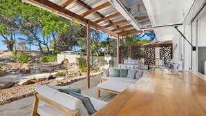 An outdoor patio with a wooden table and seating, a grill, and a view of the surrounding landscape.