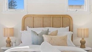 A bed with a rattan headboard, multiple pillows, and two bedside lamps on white nightstands.