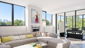 Ein modernes Wohnzimmer mit einem Ecksofa, einem Klavier und einem großen Fenster mit Blick auf die Stadt.