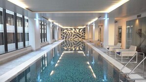 Ein moderner, überdachter Schwimmbereich mit wellenförmigen Wänden, Glastüren und Liegestühlen.