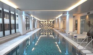 Une piscine intérieure moderne avec un mur aux lignes ondulantes, des portes vitrées et des chaises longues.