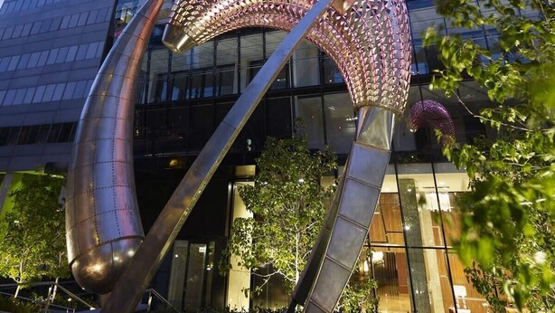 Ein modernes Gebäude mit Glasfassade und einer markanten Metallskulptur davor.
