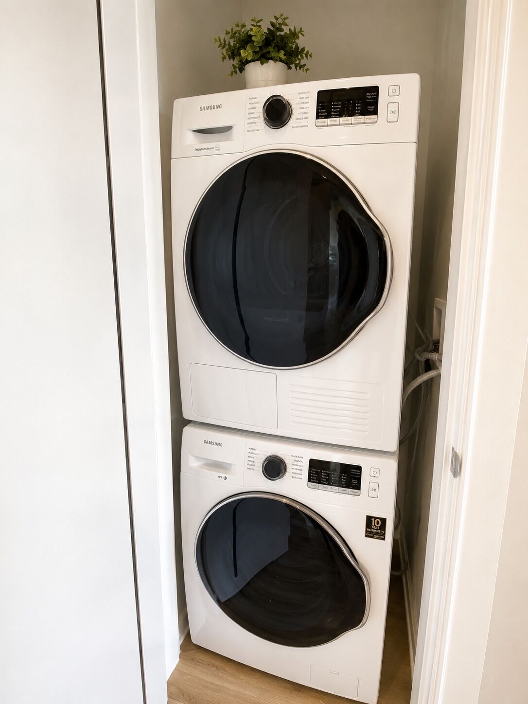A stacked washer and dryer unit in a corner with a potted plant on top.
