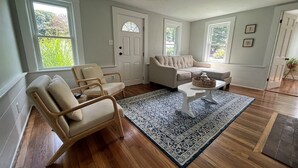 A living room with a wooden floor, two beige sofas, a white coffee table, and a patterned rug. - Charming Retreat - Central A/C, Firepit, Walk to Downtown (Falmouth)