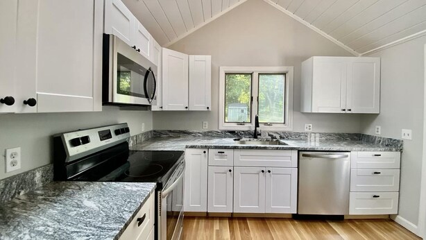 A modern kitchen with white cabinets, a black stove, granite countertops, and a skylight. - Charming Retreat - Central A/C, Firepit, Walk to Downtown (Falmouth)