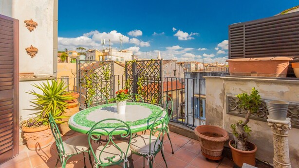 Une terrasse sur le toit, avec une table ronde et des chaises, des plantes en pot et une vue sur le paysage urbain.