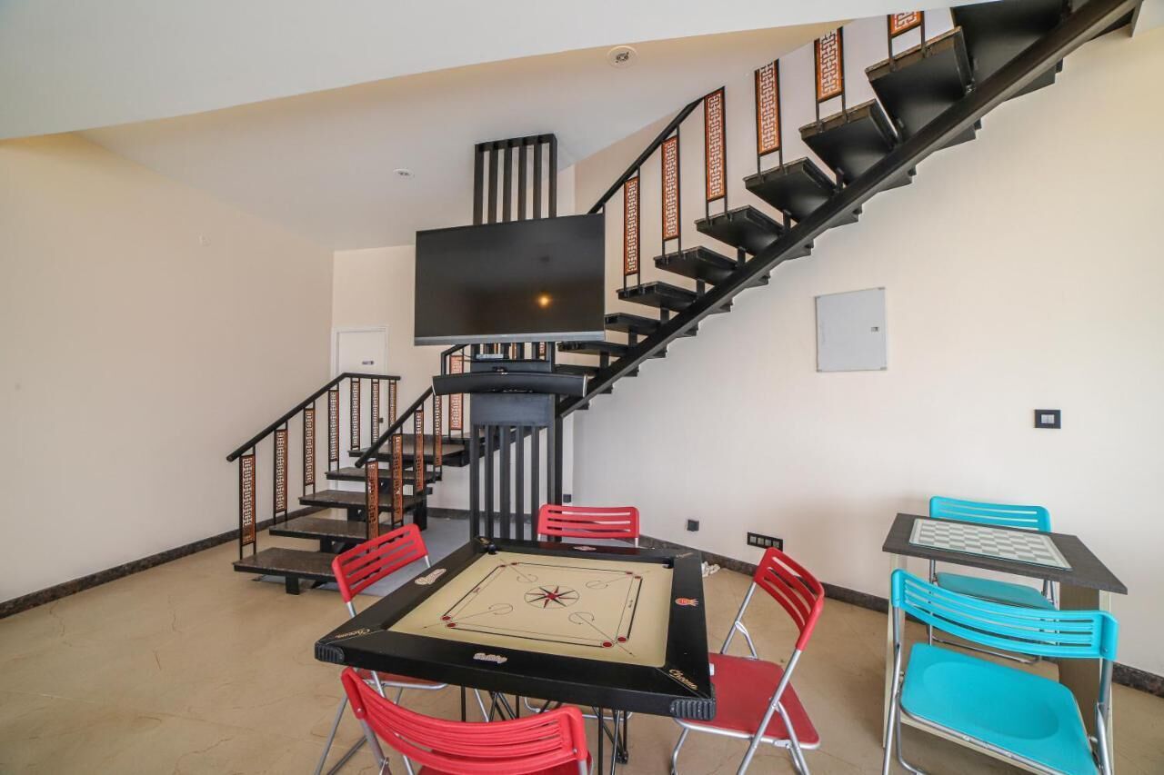 A room with a black table and chairs, a TV mounted on the wall, and a staircase with black railings.