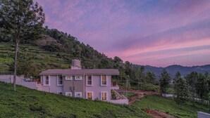 A two-story house with a flat roof, surrounded by lush green hills and trees. - Penta Peak By Indostays (Kotagiri)