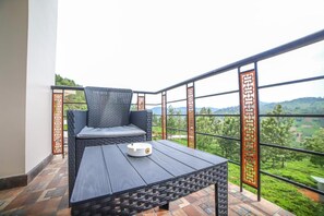 A balcony with a wicker chair and a table, overlooking a lush green landscape. - Penta Peak By Indostays (Kotagiri)