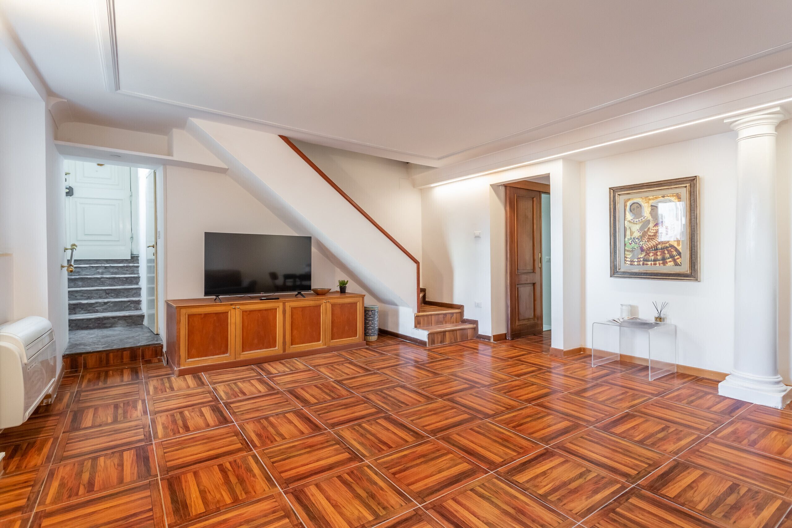 Un vaste espace de vie doté d’un plancher en bois, d’un escalier, d’une télévision et d’une œuvre d’art encadrée accrochée au mur.