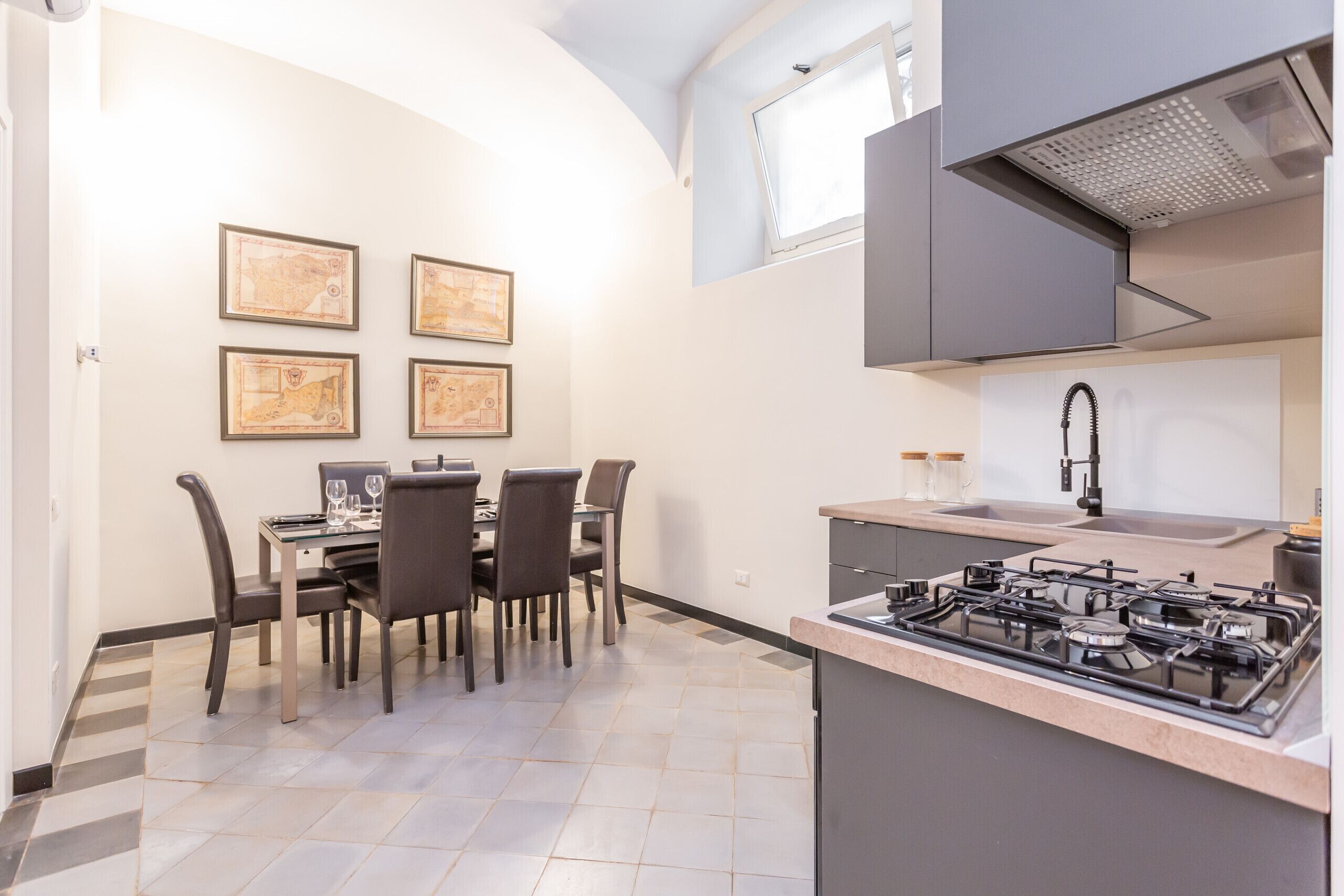 A modern kitchen with a gas stove, a dining area with four chairs, and framed artwork on the wall.
