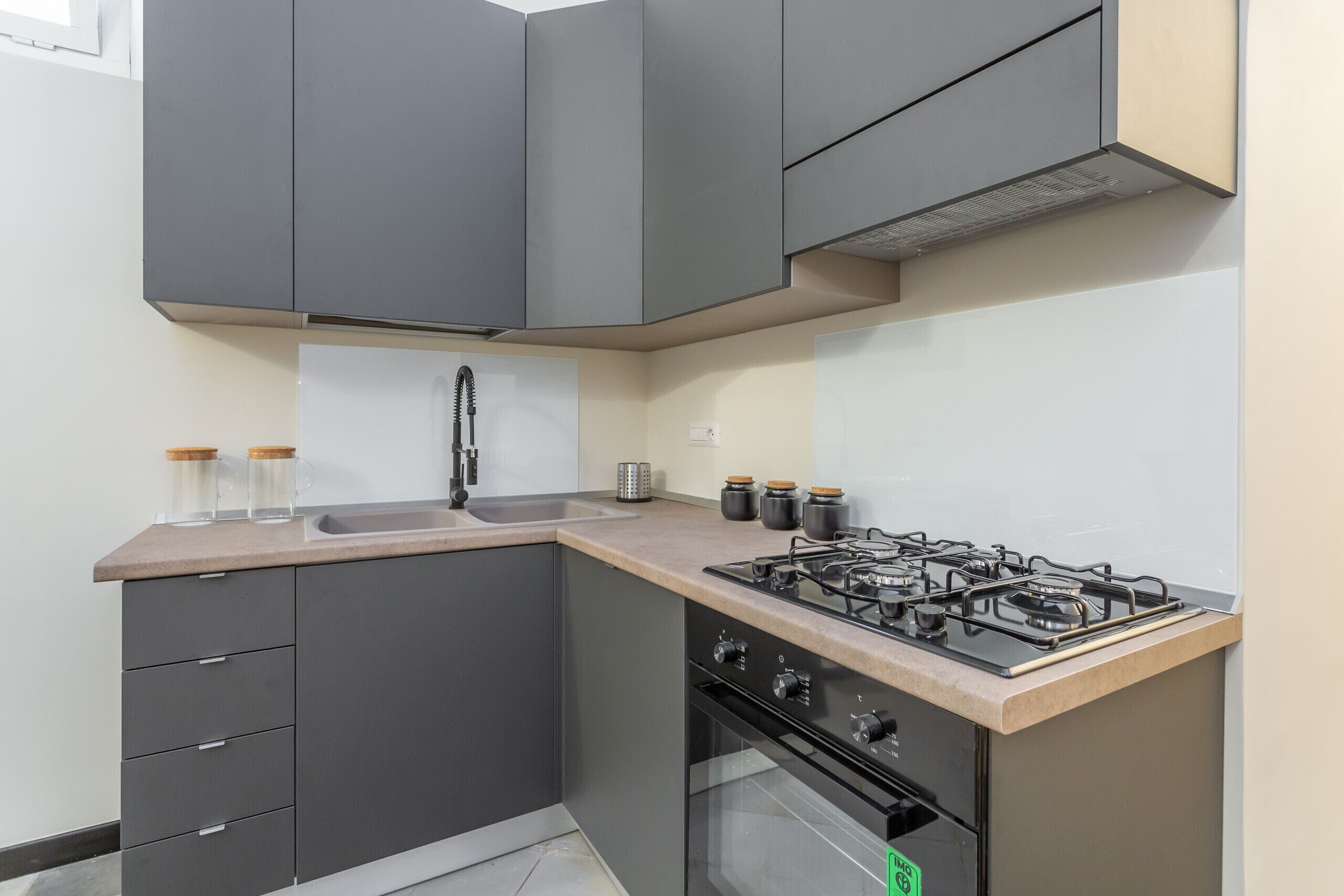Une cuisine avec des meubles de couleur grise, une cuisinière à gaz, un évier et un four encastré.