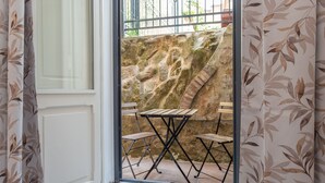 Une pièce donnant sur un mur de pierre, avec une fenêtre ornée de rideaux et une petite table accompagnée de deux chaises.