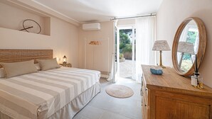 Ein Schlafzimmer mit Bett, Nachttisch, Lampe, Kommode, Spiegel und einer offenen Tür, die auf einen Balkon führt.