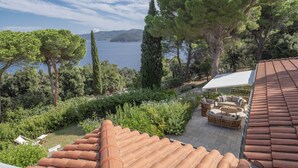 Eine Terrasse mit Terrakotta-Dachziegeln, Gartenmöbeln und Blick auf das Meer und die Berge.