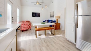 Une cuisine moderne avec des meubles blancs, un réfrigérateur en acier inoxydable, une table à manger en bois avec des bancs et un ventilateur de plafond.