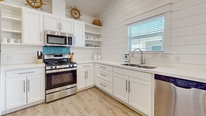 A modern kitchen with white cabinetry, stainless steel appliances, and a window with blinds. - OTC6 Golf Cart Included, Pet Friendly, Shared Pool, Parking for 1 Vehicle (Port Aransas)