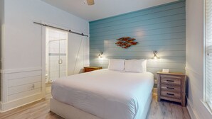 A bedroom with a large bed, a ceiling fan, a nightstand, and a wall-mounted light fixture. - OTC6 Golf Cart Included, Pet Friendly, Shared Pool, Parking for 1 Vehicle (Port Aransas)