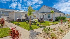 Una zona residencial con casas, una parrilla, mesas de picnic y un césped bien cuidado.